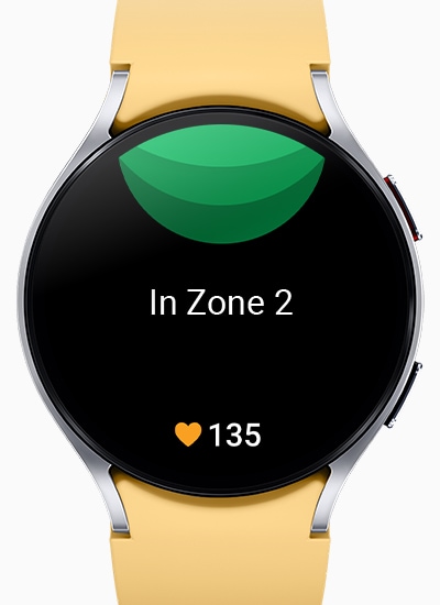 Se puede ver el Galaxy Watch6 mostrando la pantalla personalizada de la zona de frecuencia cardíaca, con el texto “En la zona 2” en el centro y el número 135 junto a un ícono de corazón en la parte inferior.