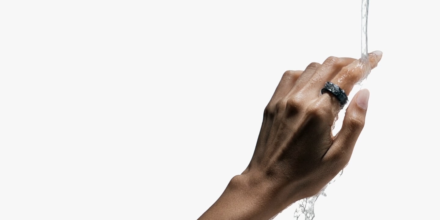 En hand som bär en Galaxy Ring kan ses. En vattenström faller på handen för att illustrera ringens vattenresistens.